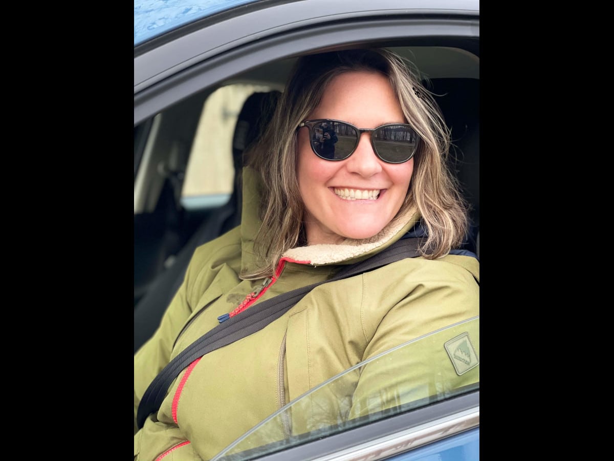 Woman wearing sunglasses smiling while sitting in a car.