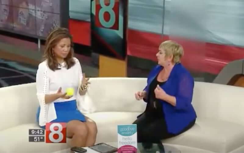 Two women having a discussion on a television set with one gesturing mid-conversation.