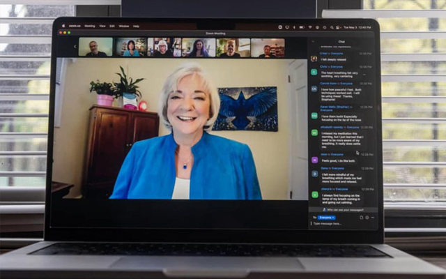 Laptop screen displaying a video conference call with multiple participants, highlighting a smiling woman in a blue top.