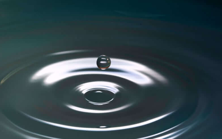 A single water droplet suspended above a calm surface, creating ripples.