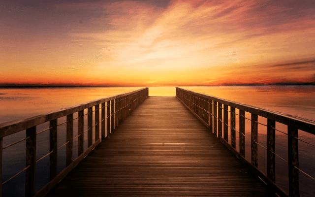 Wooden pier extending into calm waters during a vibrant sunset.