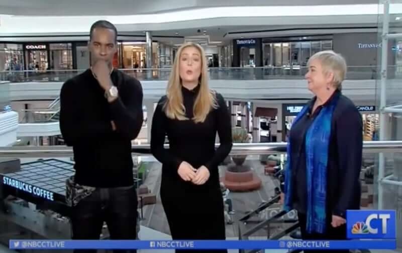Three individuals in a mall setting during a television broadcast segment.