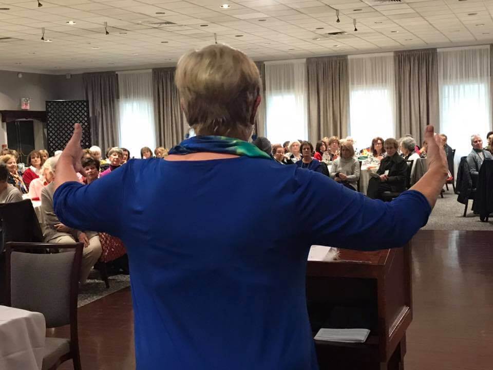 A speaker gesturing to an audience in a seminar hall.