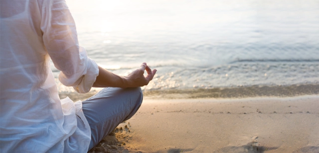 Person meditating on the beach at sunset for stress relief.